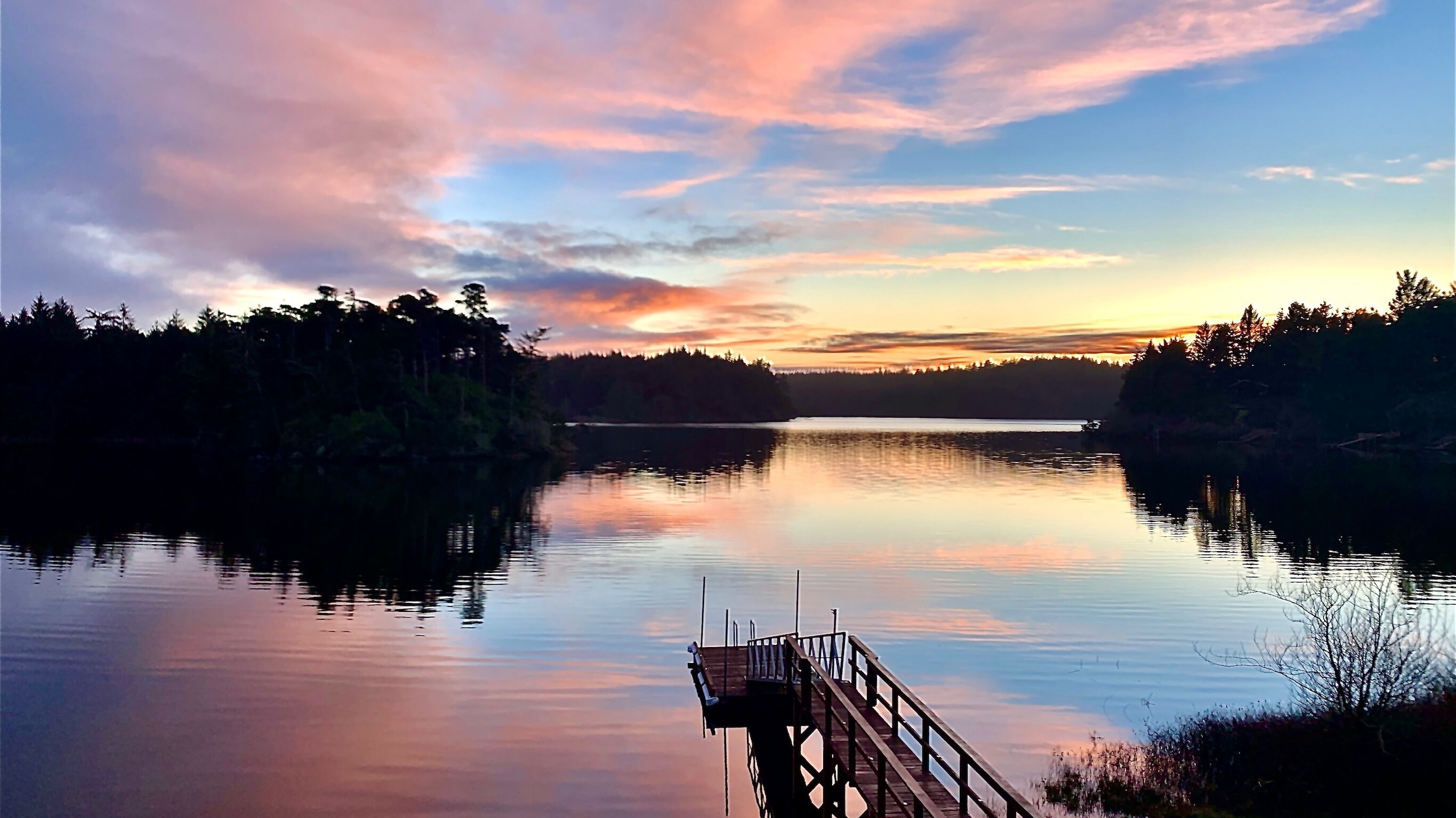Un lac paisible, avec une jetée en bois qui s’avance sur l’eau.