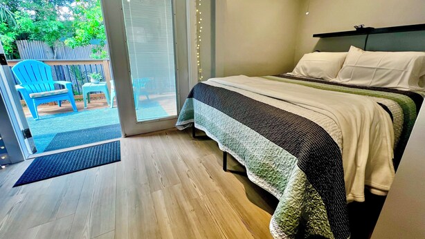 Une chambre à coucher avec un lit, une fenêtre avec des stores, une porte donnant sur un balcon et un luminaire au plafond.