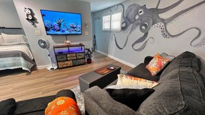 Un salon comprenant un canapé, un téléviseur, une fresque murale, un lit et un meuble en bois.