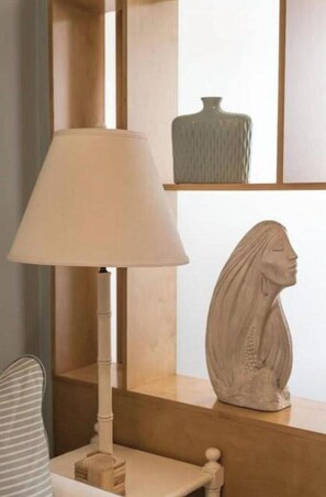 Une lampe avec un abat-jour blanc, une sculpture en bois et un vase posés sur une étagère.