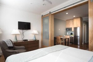 A hotel room with a bed, a desk, a chair, a TV, and a kitchenette.