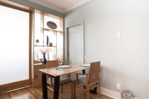 A dining area with a wooden table and chairs, a vase with dried flowers, and a door with a decorative plate.