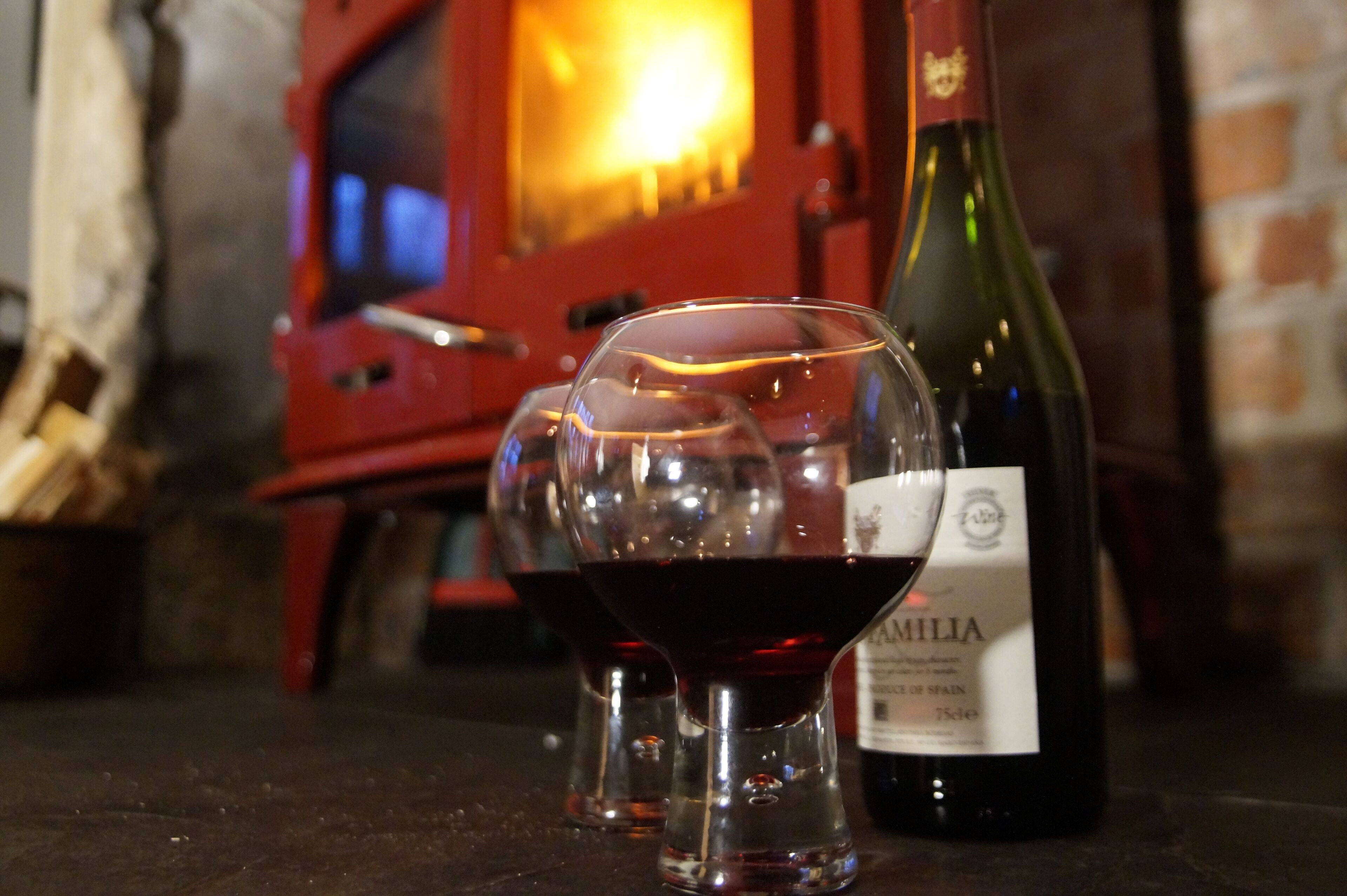 A wine bottle and two glasses on a table with a brick wall and a red cabinet in the background.
