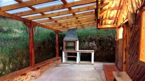 An outdoor patio with a brick oven, wooden pergola, and a bench.