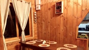 A wooden dining table with placemats, a bench, a window with curtains, and a shelf with toys.