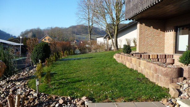 Un quartiere residenziale con un prato curato, un vialetto in pietra e una casa in mattoni con un balcone.