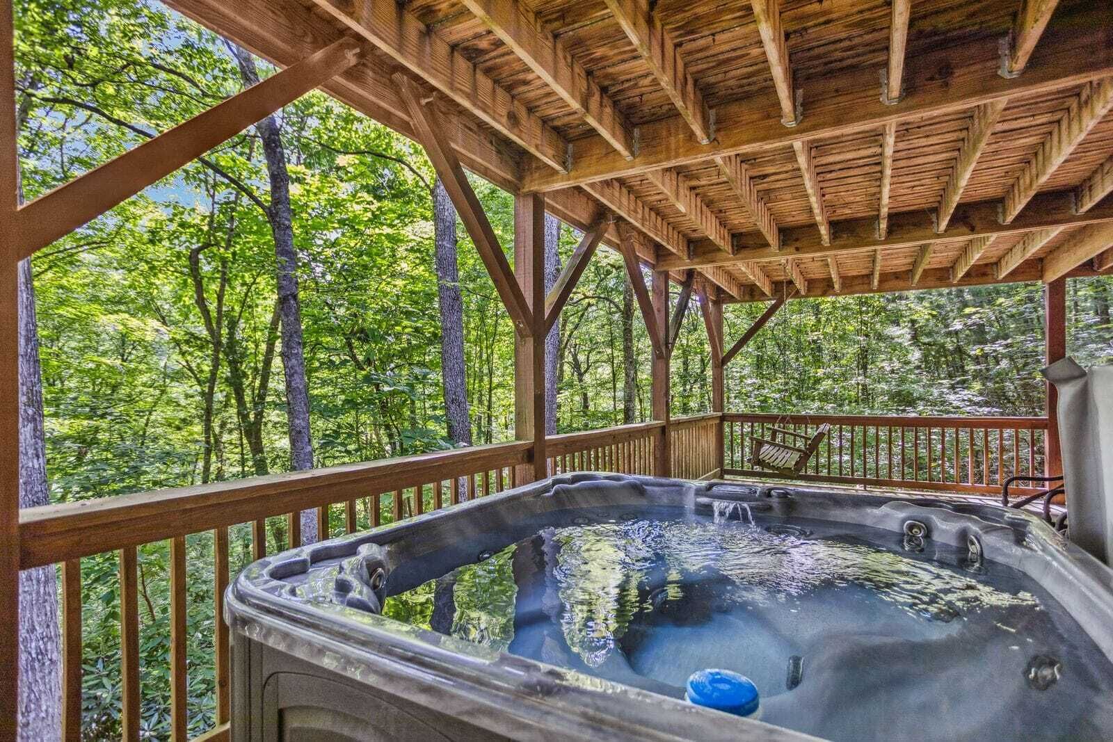 Un jacuzzi bajo un porche de madera con vistas a un bosque.