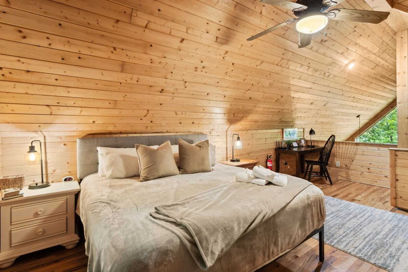 Una habitación acogedora de madera con una cama, mesitas de noche, un escritorio y una silla.
