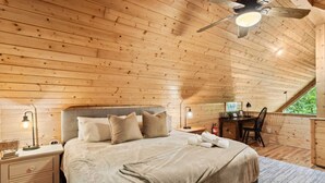 Um quarto acolhedor de madeira, com uma cama, mesas de cabeceira, uma escrivaninha e uma cadeira.
