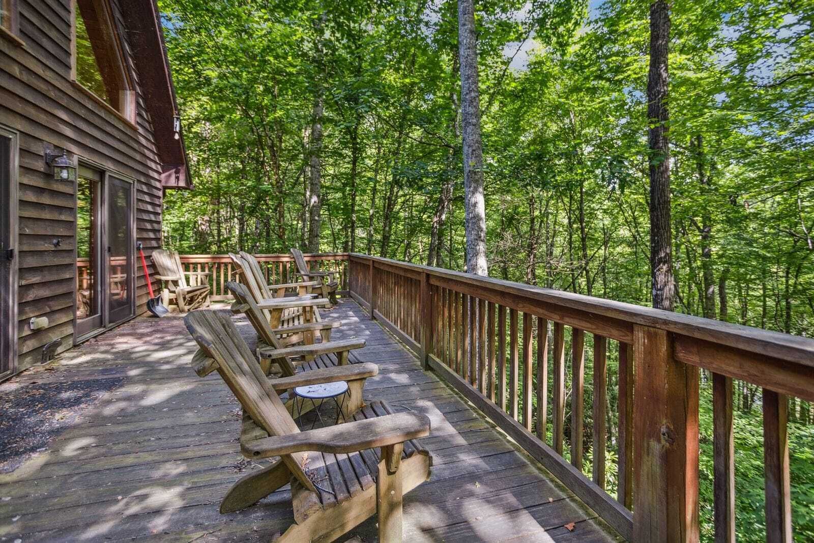 Une terrasse en bois, avec des chaises et une table, entourée d’une forêt.