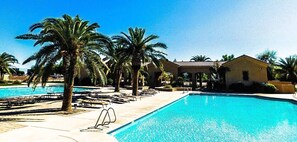 Piscina com cadeiras de sol e palmeiras, cercada por edifícios.