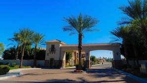 A gated entrance with a central archway, surrounded by palm trees and a paved driveway leading to a residential area. - Country Club 1104, heated pool, 1000 feet from Golfland Sunsplash Amusement Park (Mesa)