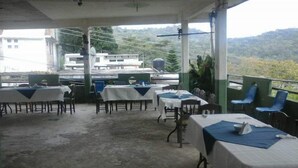 An outdoor dining area with tables and chairs, a view of buildings and hills in the background.