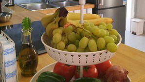 A kitchen with a stainless steel refrigerator, a sink, and a countertop with a bowl of fruit, vegetables, and a bottle of oil. - Betty's Villas (Pyrgos)
