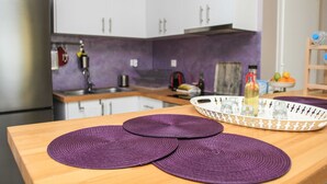 A kitchen with a wooden table, purple placemats, and a tray with glasses and bottles. - Betty's Villas (Pyrgos)