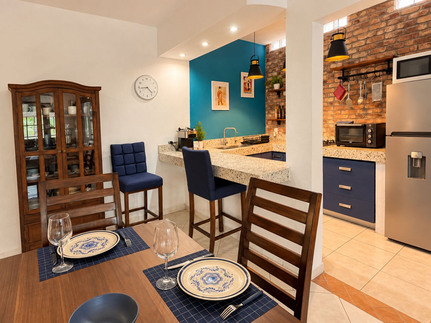 A modern kitchen with a blue accent wall, a dining area with blue upholstered chairs, and a built-in wooden cabinet.