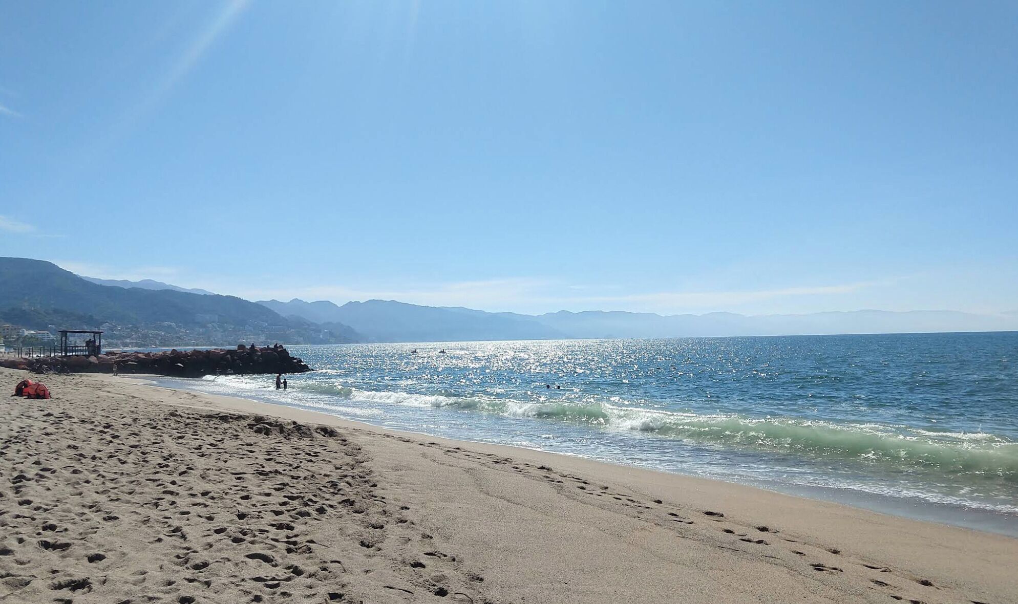 A beach with footprints, a lifeguard tower, and mountains in the background.