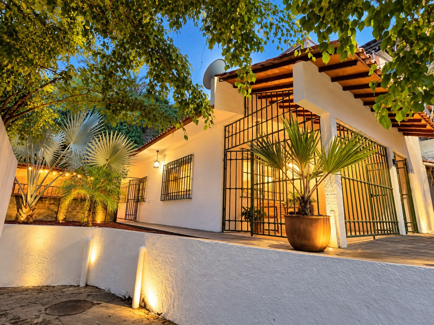 A building with a white exterior, a gated entrance, and a covered patio area with potted plants.