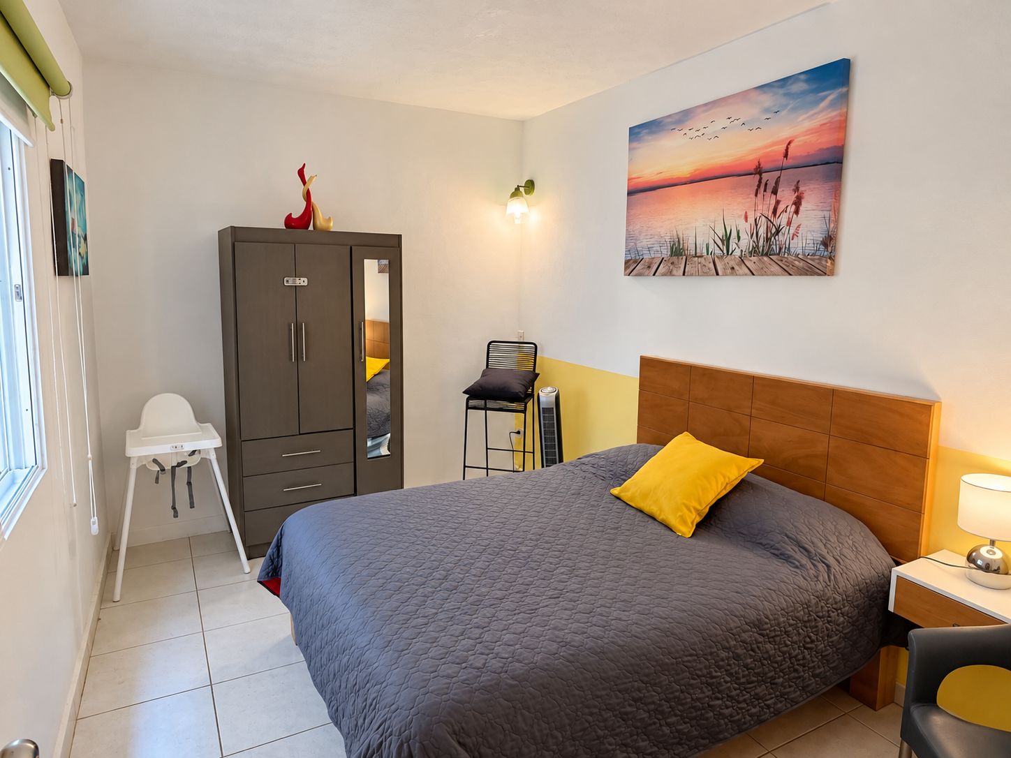 A bedroom with a bed, a wardrobe, a desk, a chair, and a painting on the wall.