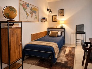 Une chambre à coucher comprenant un lit, une armoire en bois, un bureau, une chaise, un globe terrestre, une carte du monde et des lampes fixées au mur.