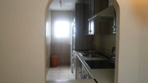 A narrow hallway leading to a kitchen with a sink, cabinets, and a window.