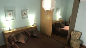 A bedroom with a bed, bedside tables, a mirror, a chair, and two framed pictures on the wall.