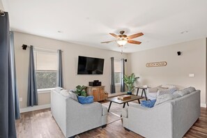 Un salon avec un canapé gris, une table basse, un téléviseur et un ventilateur de plafond.