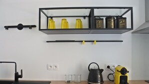 Een keuken met een zwart aanrecht, een waterkoker, een geel apparaat en een plank met gele en zwarte containers.