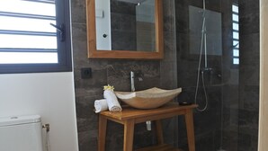 Een badkamer met een houten wastafelmeubel, een grote spiegel, een stenen wastafel en een douchecabine.