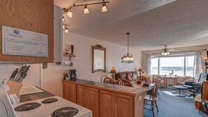 Eine Küche mit Herd, Holzschränken und einem Essbereich mit Stühlen und Tisch. An der Wand hängt ein Zertifikat und durch die Fenster ist der Blick auf den Ozean möglich.