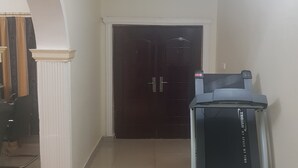 A hallway with a treadmill, a dark wooden door, and a white wall with a decorative molding. - Rayoni Guesthouse B&B (Mzuzu)