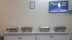 A conference room with two buffet tables, a framed certificate on the wall, and a TV displaying a show. - Rayoni Guesthouse B&B (Mzuzu)