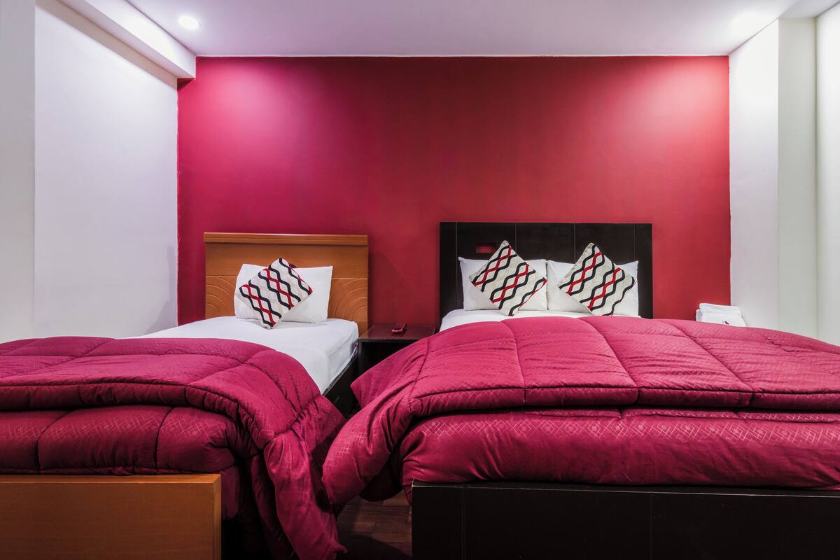 Habitación de hotel con dos camas, cada una con cubrecama y almohadas a juego en rojo. La habitación tiene una pared de acento roja y ropa de cama blanca.