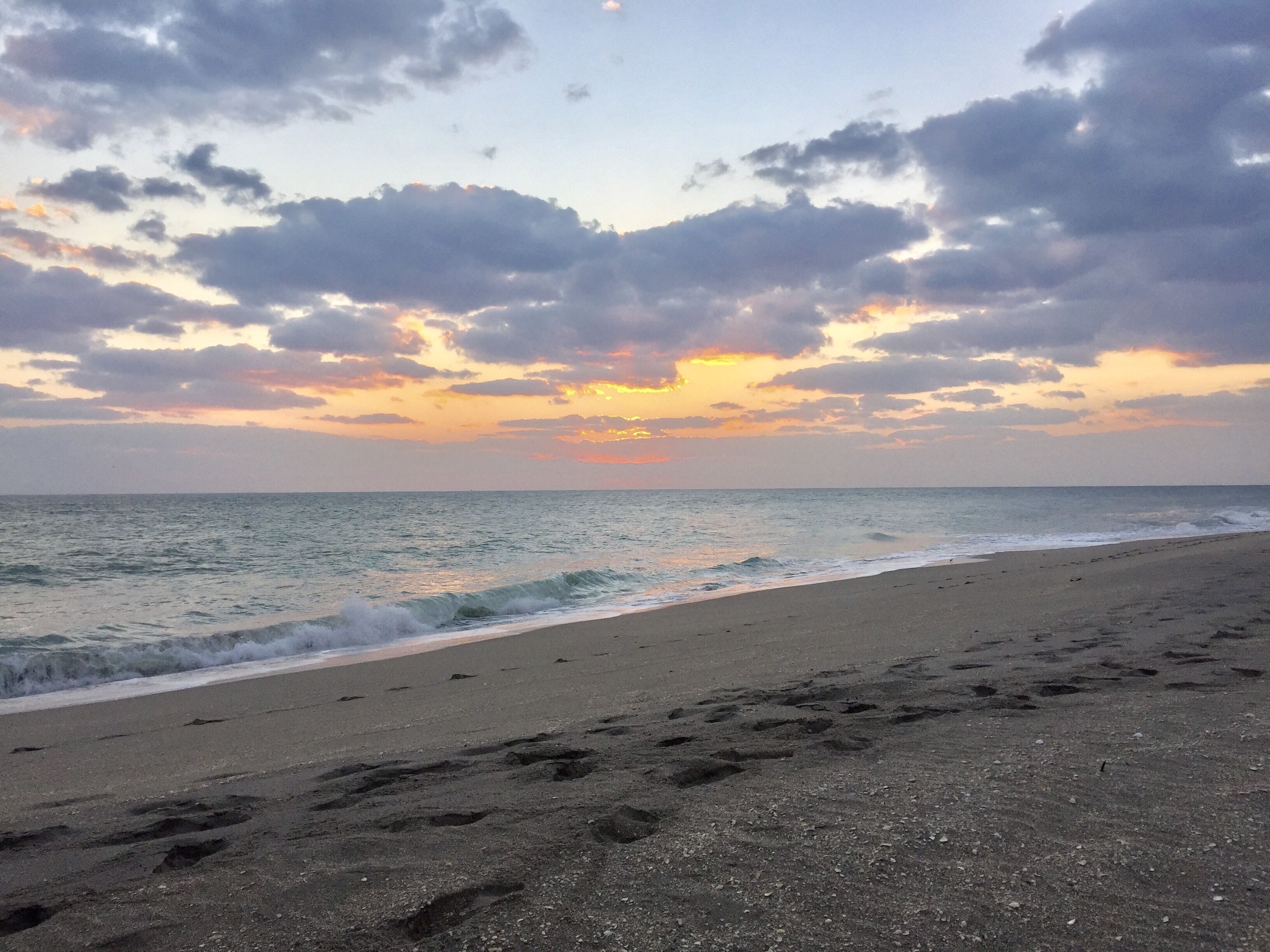Uma praia com pegadas que levam à água, céu claro e o oceano.