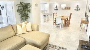 Una sala de estar con un sofá color beige, un comedor con sillas de madera y una cocina al fondo.