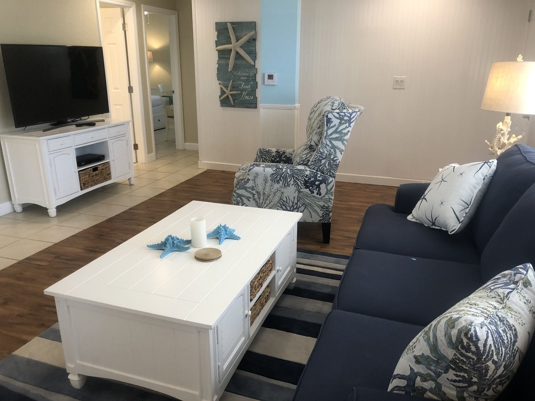 Una sala de estar con una mesa de centro blanca, un sofá azul y un sillón estampado.