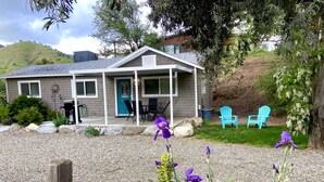 A house with a porch, outdoor seating, and a gravel driveway. - All New Remodeled Cottage (Three Rivers)
