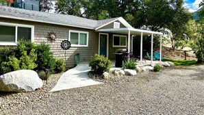 A house with a covered porch, a stone pathway leading to the entrance, and a small garden area with rocks and plants. - All New Remodeled Cottage (Three Rivers)