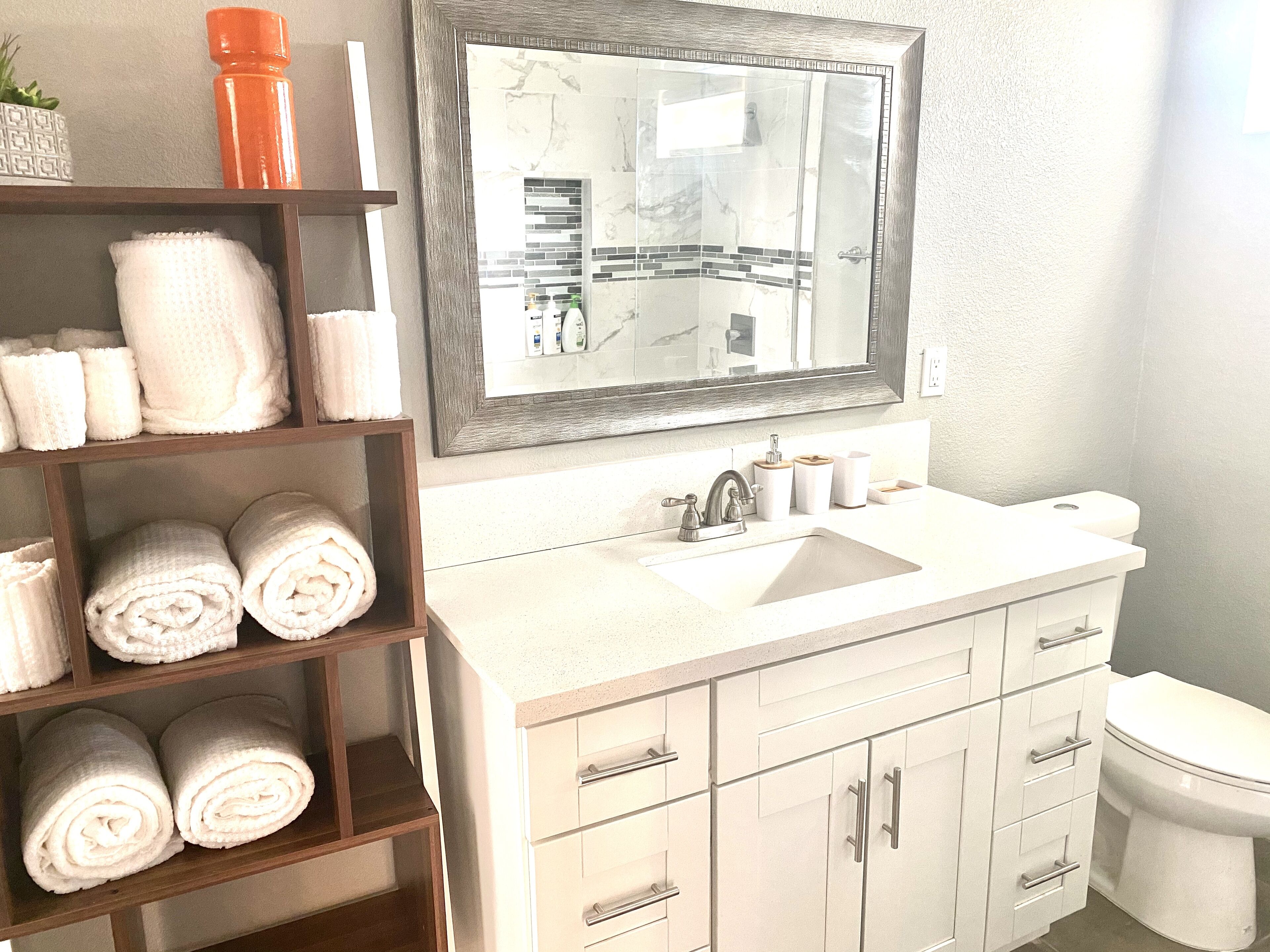 A bathroom with a white sink, a mirror, a toilet, and a towel rack with neatly folded towels.