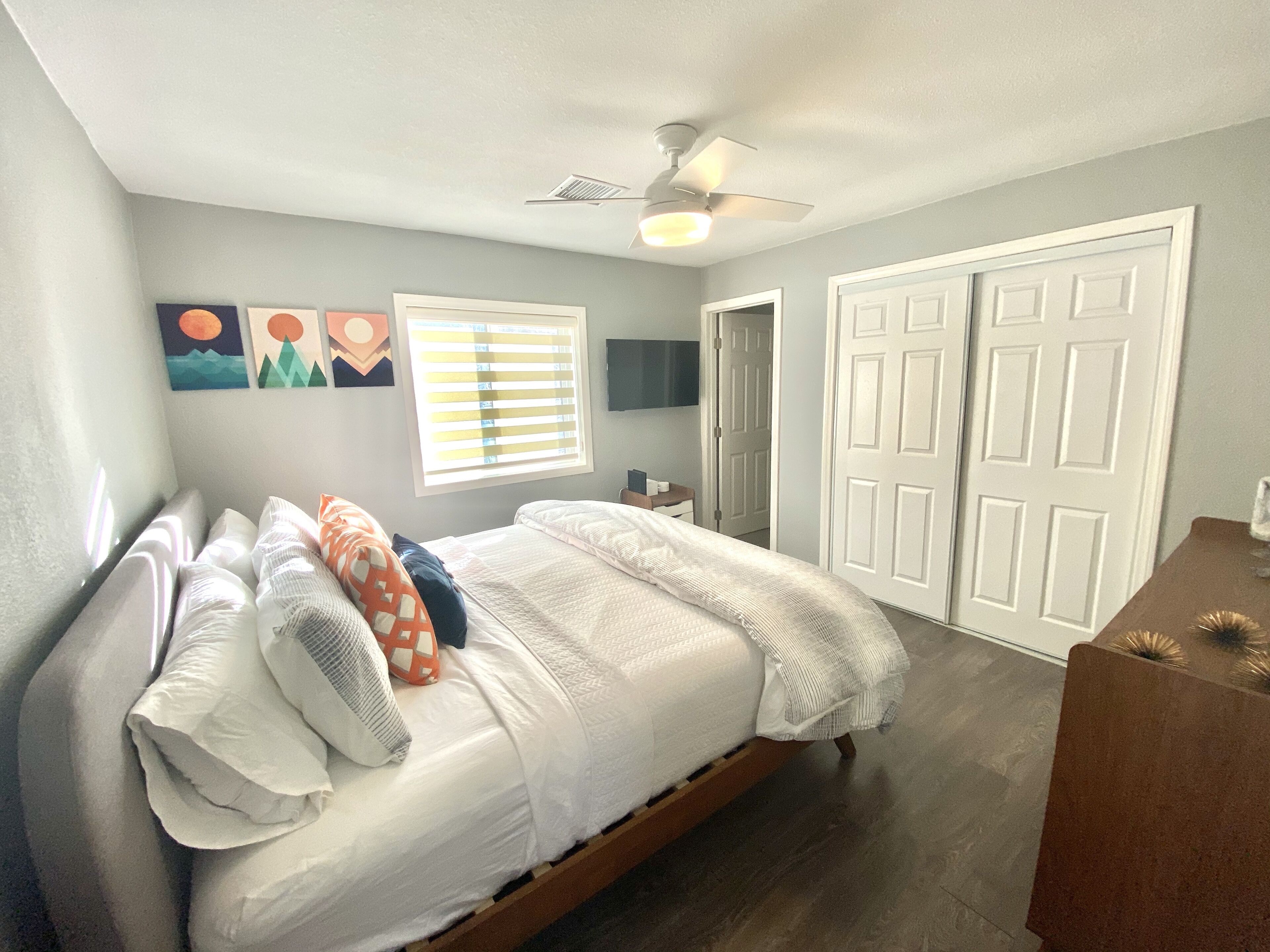 A bedroom with a bed, a ceiling fan, a window with blinds, and a door.