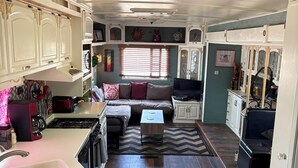 A compact RV interior with a kitchenette, a seating area with a sofa and coffee table, and a dining table.