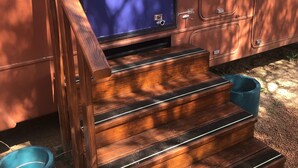 A set of wooden steps leading to a door with a window, a metal handle, and a small sign.