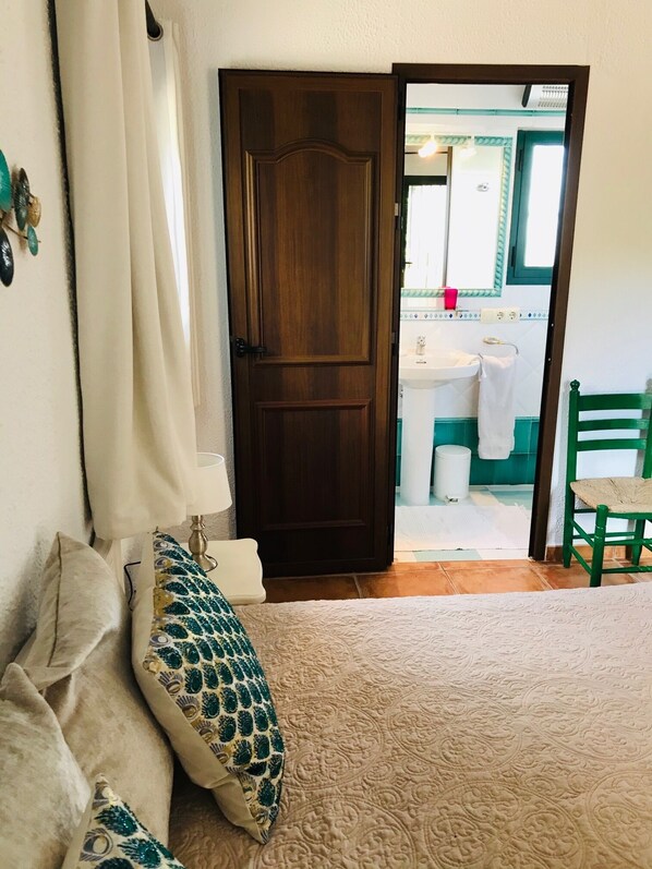Een slaapkamer met een bed, een groene stoel, een houten deur en een zichtbare badkamer door een open deur.