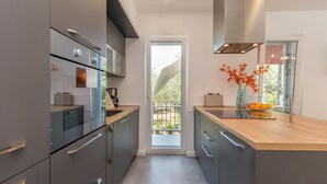 Une cuisine moderne avec des meubles de couleur grise, un plan de travail en bois et une vue sur l’extérieur grâce à une porte vitrée.