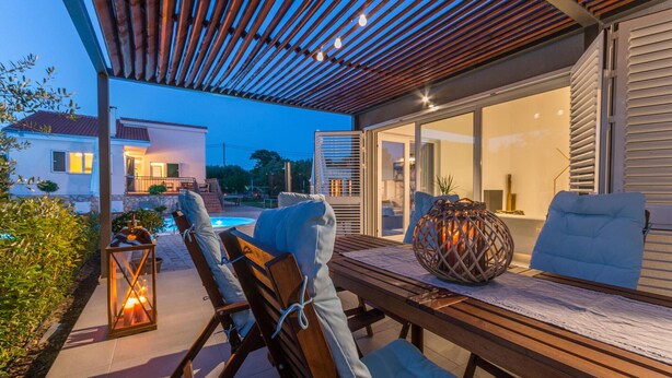 Une terrasse extérieure avec une table en bois, deux fauteuils de jardin, une lanterne et une sphère décorative.