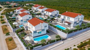 Un complejo residencial moderno con varias casas de dos pisos, cada una con piscina y zonas de estar al aire libre.