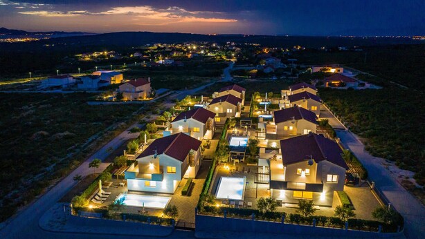 Un barrio residencial con casas modernas, una piscina y una calle bien iluminada al anochecer.