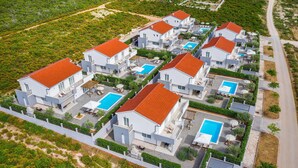 Un conjunto residencial con varias casas, cada una con piscina y tejado de tejas rojas.
