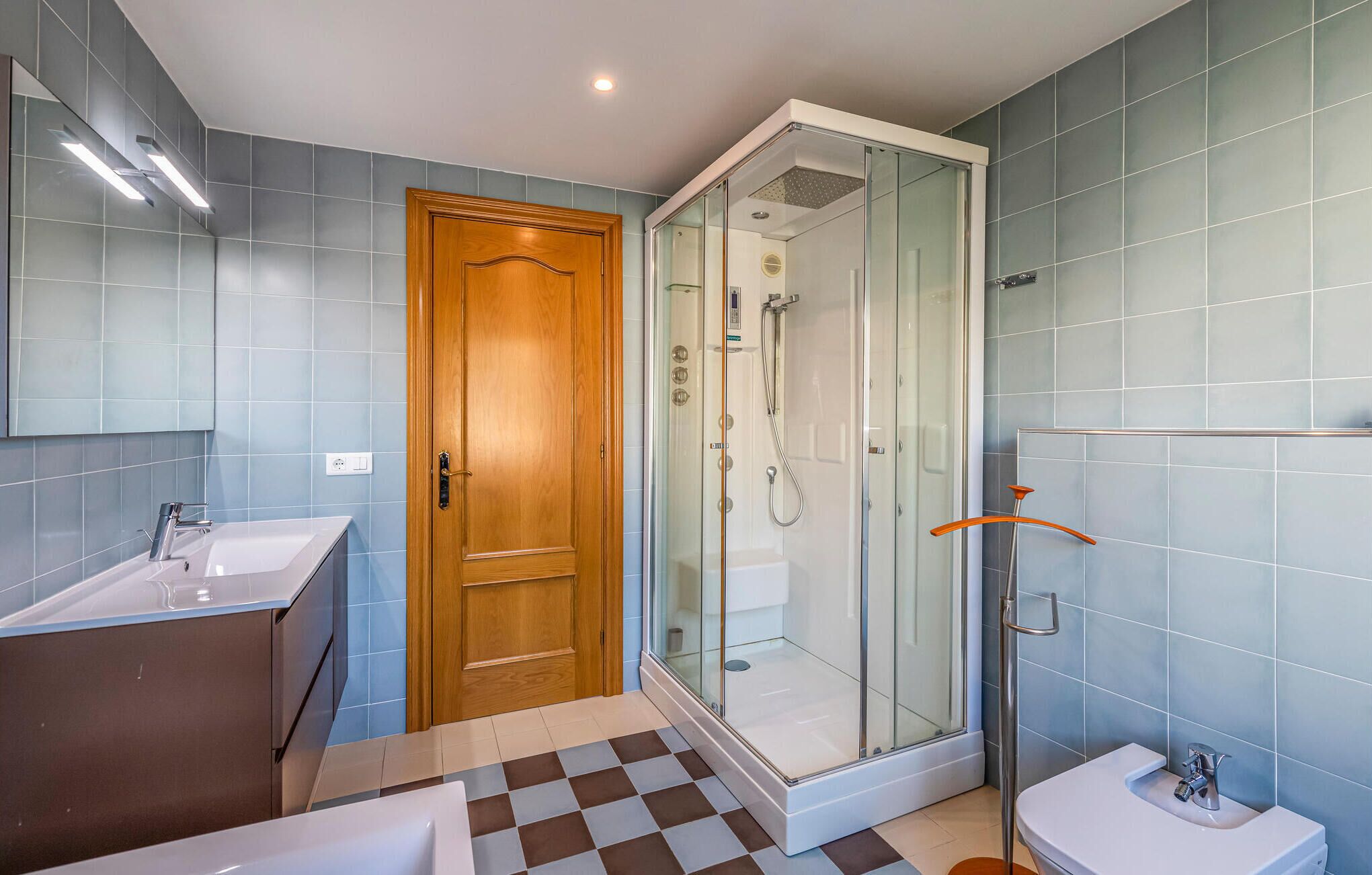 A modern bathroom with a glass-enclosed shower, a wooden door, and a checkered floor.