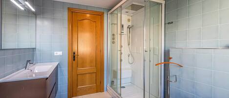A modern bathroom with a glass-enclosed shower, a wooden door, and a checkered floor.